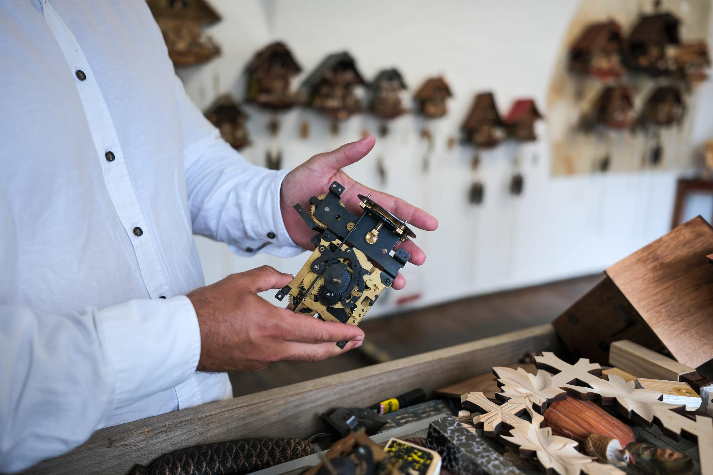Ein mechanisches Schwarzwälder Kuckucksuhrwerk aus Messing und Stahl, in zwei Händen gehalten, davor die Uhrenwand im Gewölbe der InnResidenz in Passau.
